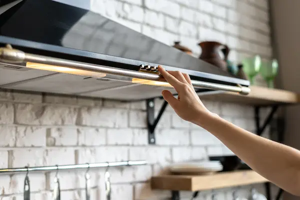 Cropped View Woman Hand Selecting mode of a range hood exhaust.