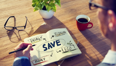 Man in business attire holding pen and staring down at energy saving diagram drawn in notebook.