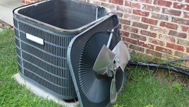 Central AC condenser unit with cover removed for cleaning and maintenance beside red brick wall.