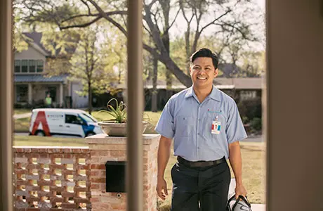 Smiling male Aire Serv technician arriving for residential service appointment with branded van parked in background.