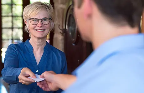 Smiling middle-aged female customer receiving bill from male Aire Serv technician.