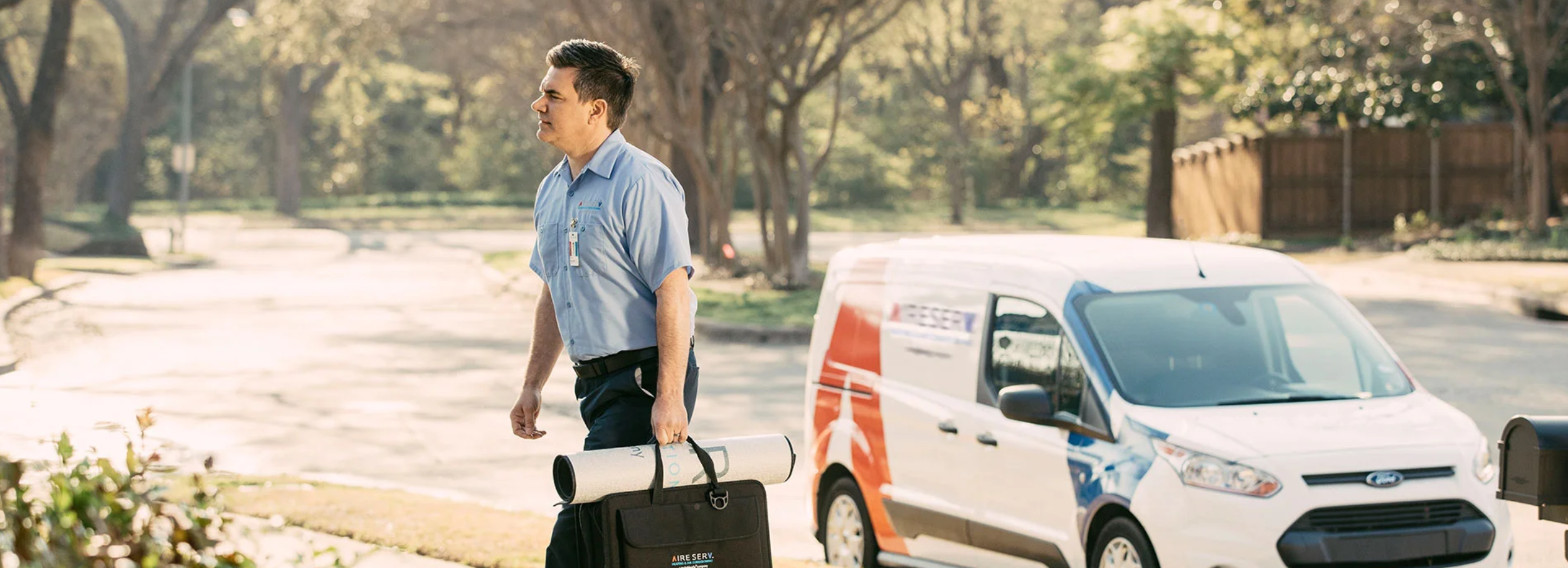 Serious male Aire Serv technician in branded blue collared shirt arriving for residential service call with tool bag.