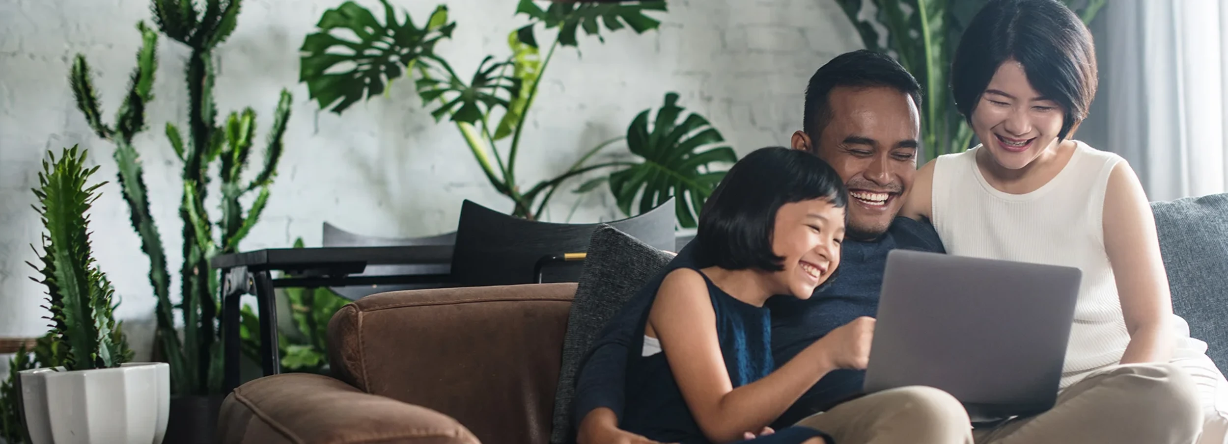 Smiling dad, daughter, and mom sitting on the couch looking at a laptop.