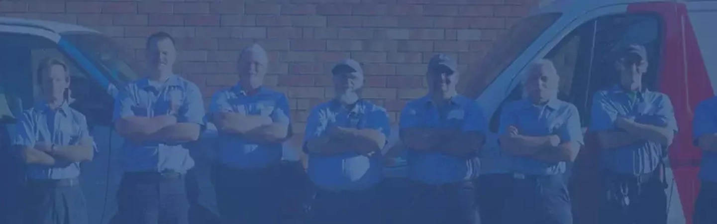 Row of Aire Serv technicians with arms crossed standing between pair of branded vans.